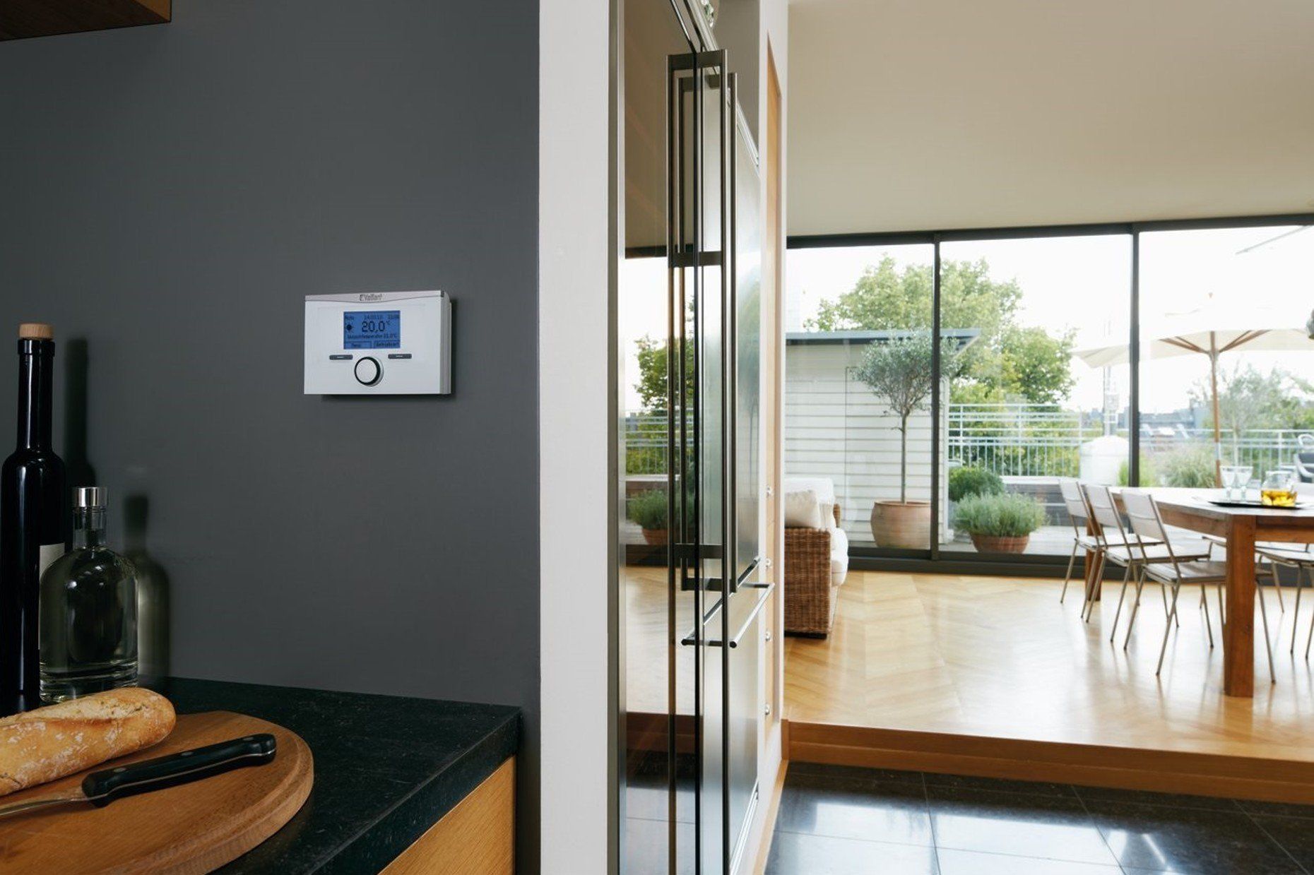 Thermostat on a gray kitchen wall, with a view of a dining area with large windows.