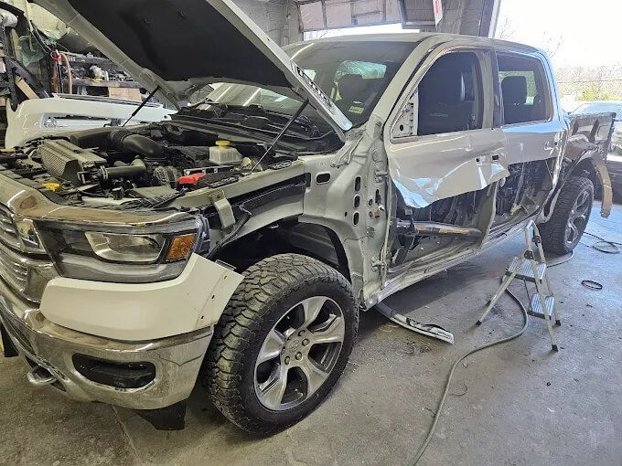 White pickup truck with severe side damage in a repair shop, hood open and parts exposed
