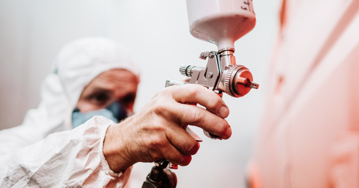 Painter spraying white paint on a wall with a spray gun, wearing protective gear and face mask.