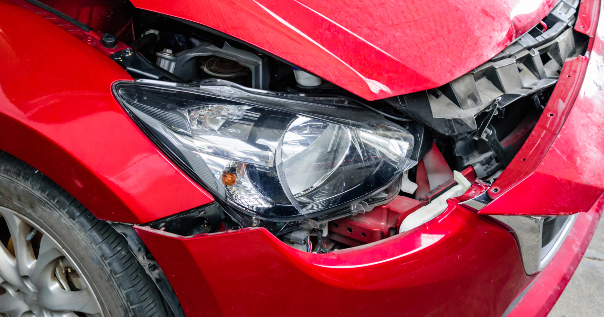 Damaged red car front end with a crushed headlight and bent bumper
