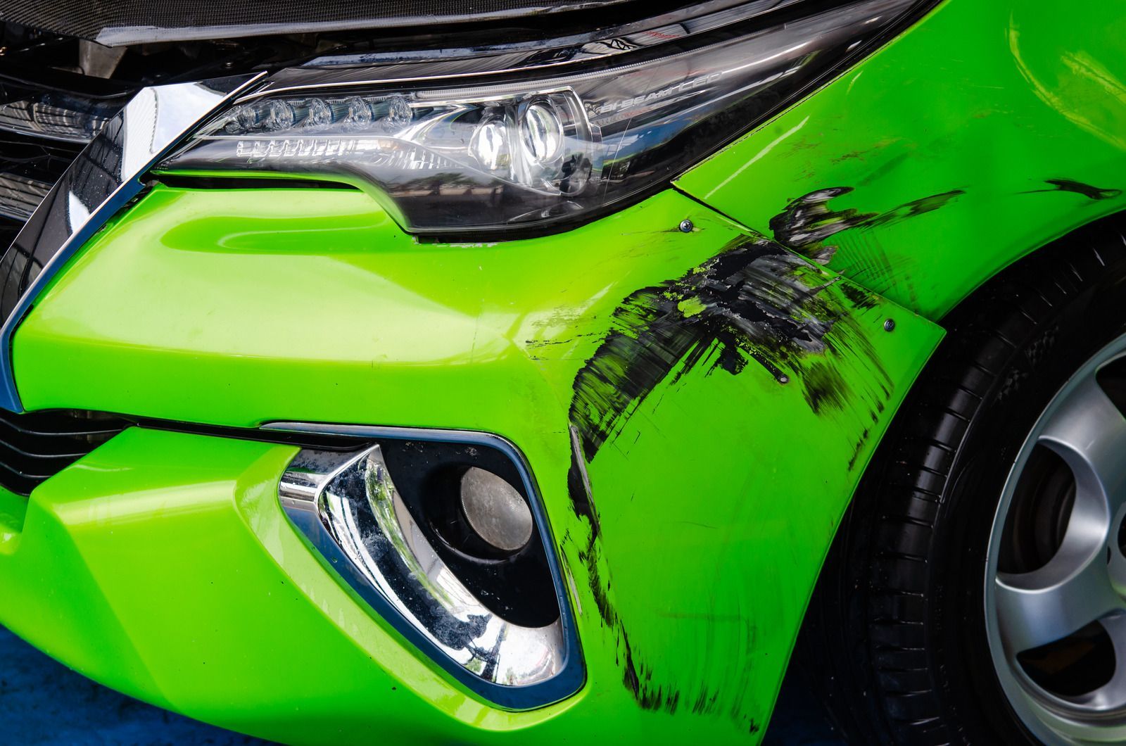 Bright green car front bumper with black scrape damage and scratched wheel arch
