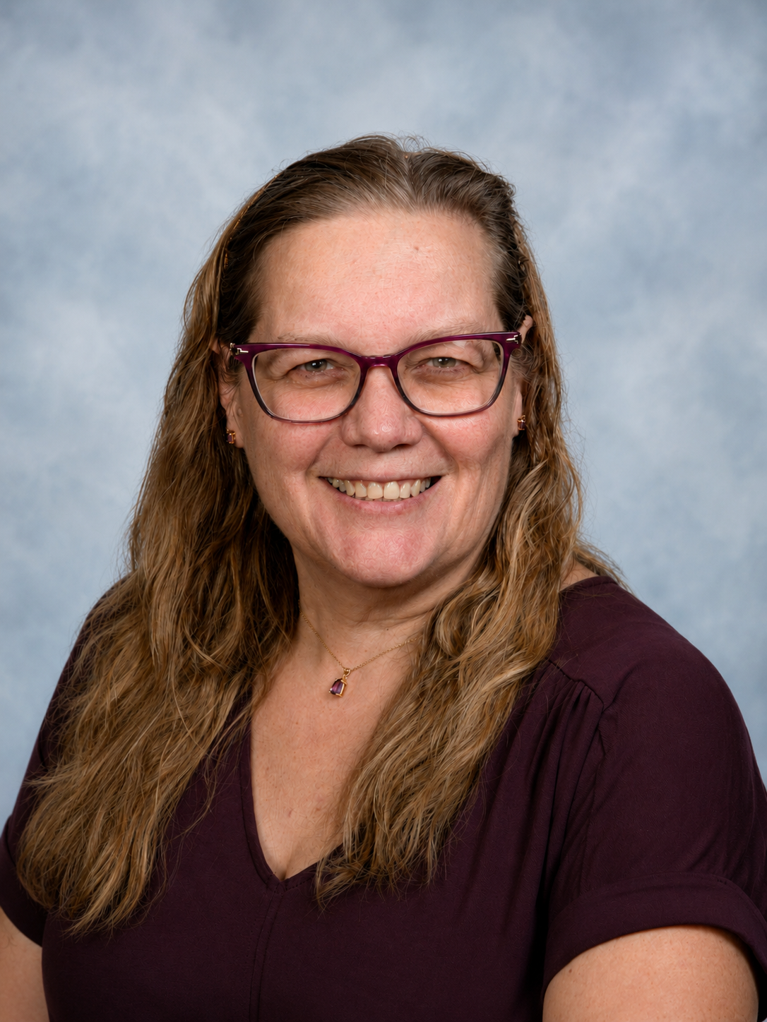 Woman wearing glasses smiles at the camera in front of a brick wall.