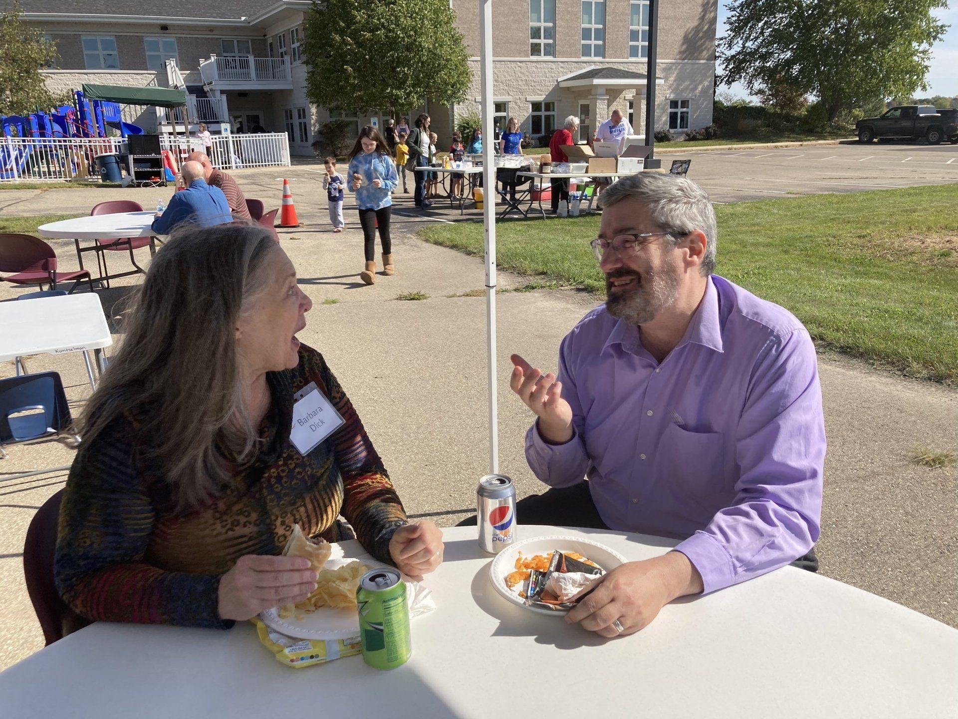 Two people seated at a table outside, eating and conversing.