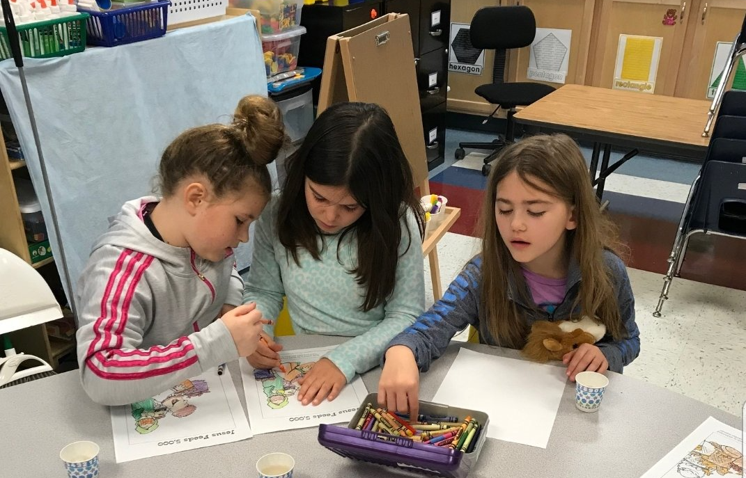 Three girls at a table working on a craft project with colorful materials and drawings.