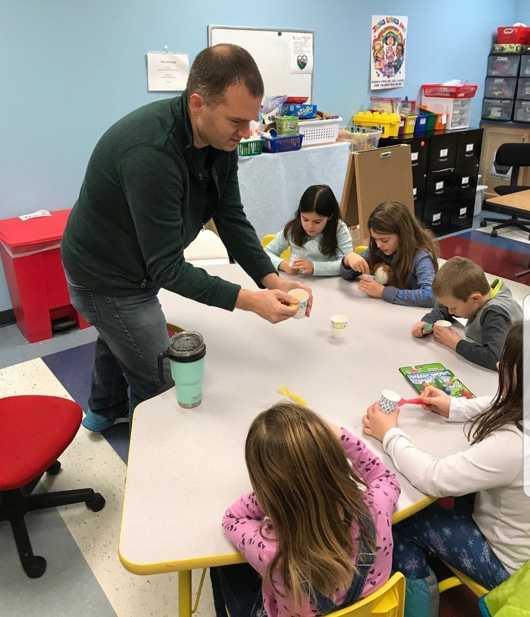 A man demonstrates an activity to children seated around a table.