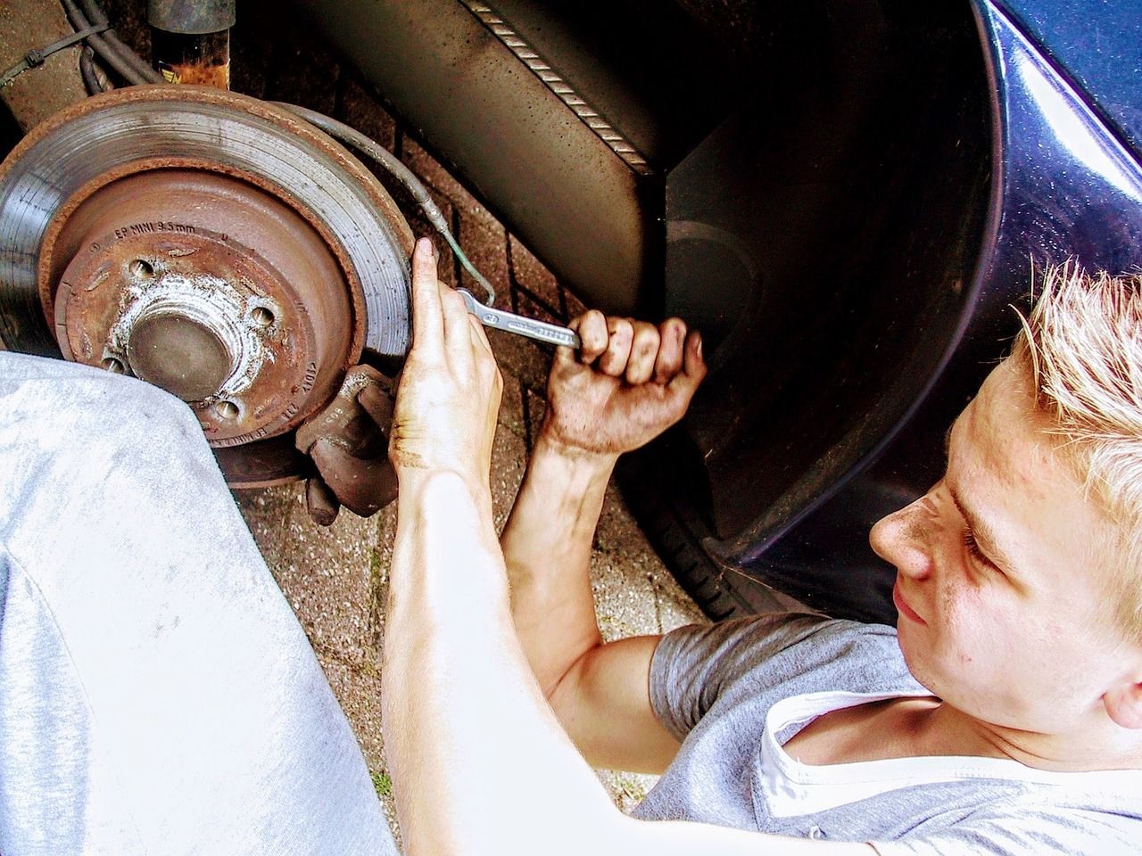 Person working on a car's brake disc with a wrench, focusing on the mechanical task outdoors.