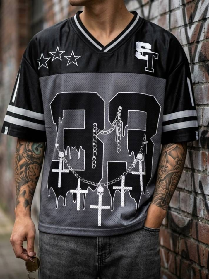 Persona con una camiseta negra estampada con cruces y estrellas plateadas, de pie sobre un fondo liso.