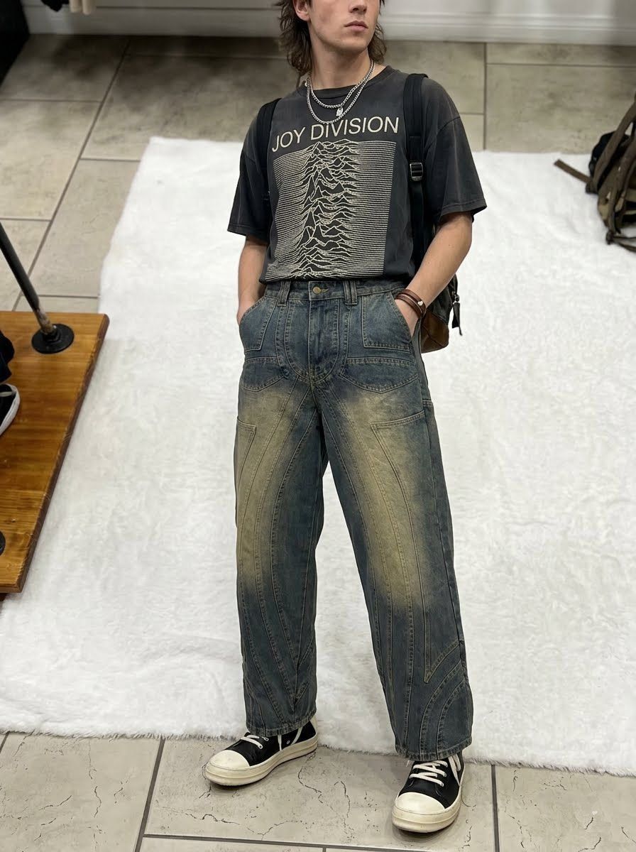 Persona con camiseta negra estampada y vaqueros azules de pie sobre una alfombra blanca en el interior de un edificio.