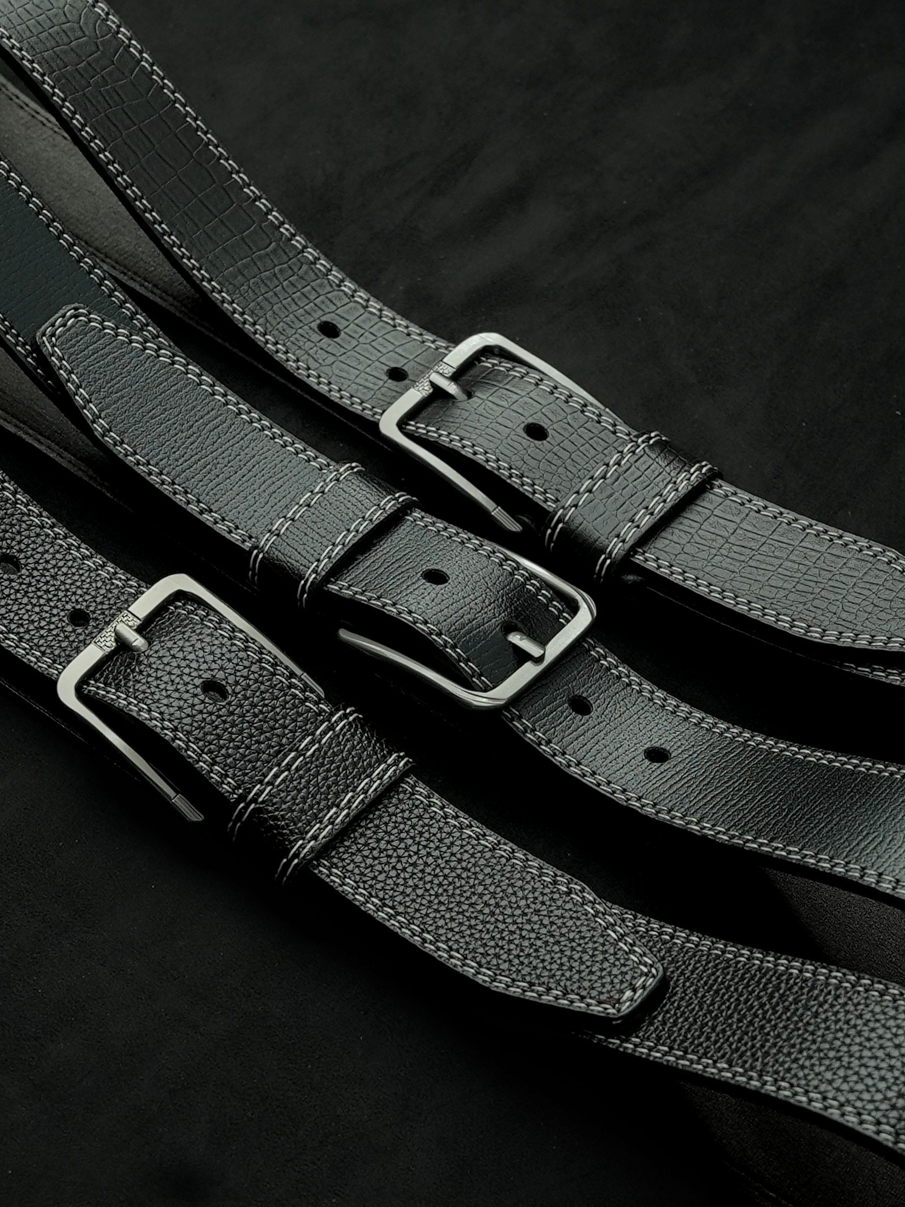 Correas de cuero negro con hebillas plateadas dispuestas sobre un fondo de tela oscura.