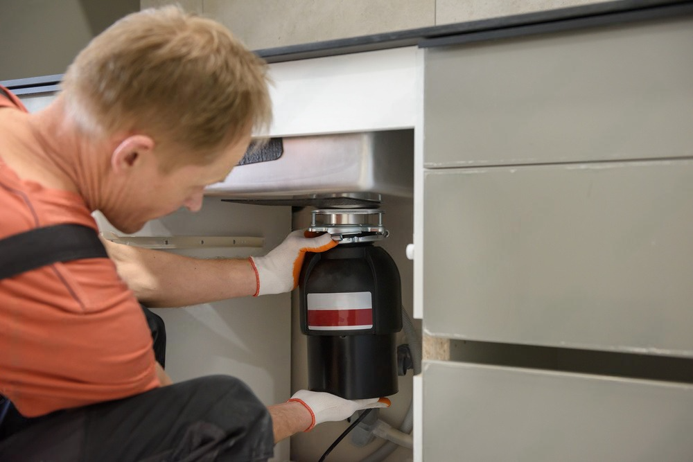 a man is fixing a garbage disposal under a sink in a kitchen .