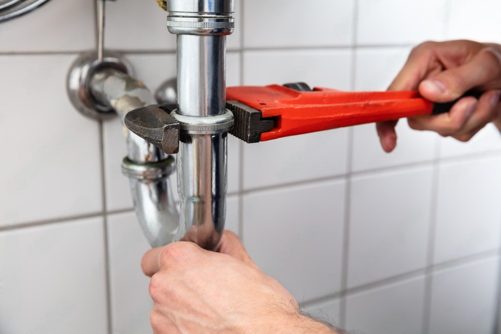 a plumber is fixing a sink pipe with a wrench .