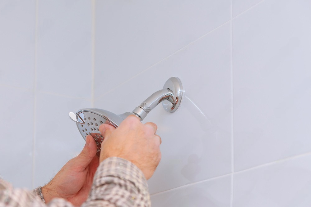 a person is fixing a shower head in a bathroom .