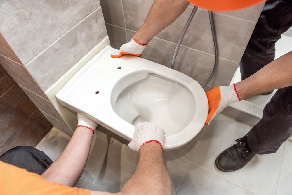 two men are installing a toilet in a bathroom .