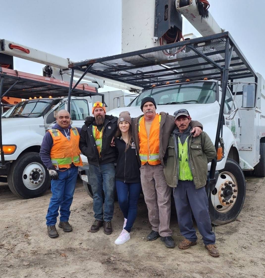 Five workers in safety vests posing in front of a utility truck on a muddy worksite