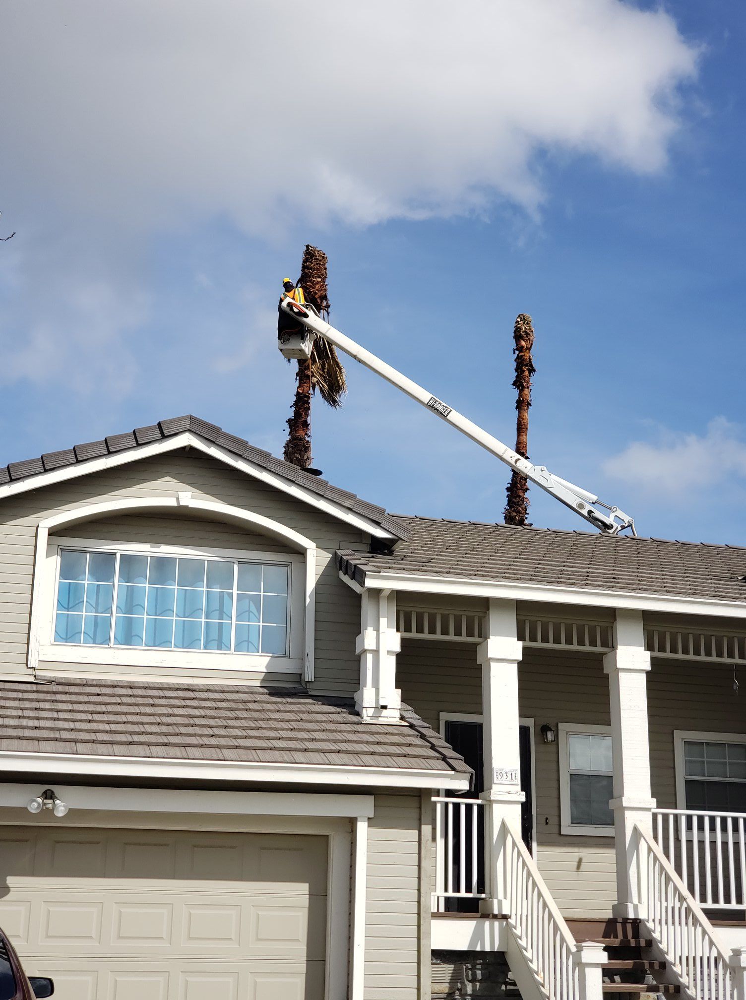 Roofers working on a suburban house roof with a boom lift against a blue sky
