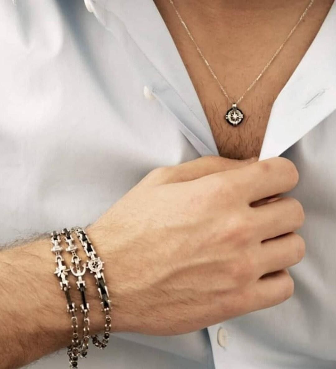 Primo piano di una persona che si sistema una camicia bianca, indossando una collana d'argento e braccialetti a catena.