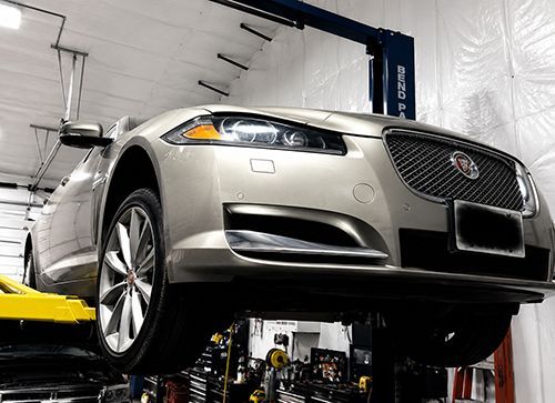 Silver Jaguar sedan raised on a car lift in an auto repair shop, front view