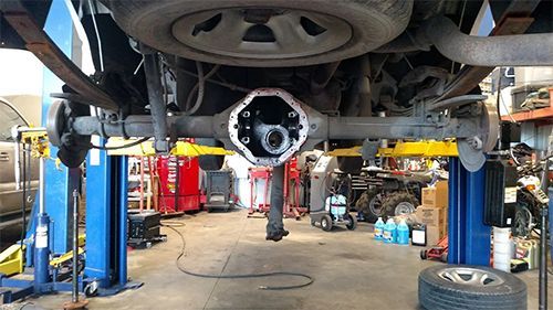Undercarriage of a car lifted in an auto repair shop, with tools and equipment below.