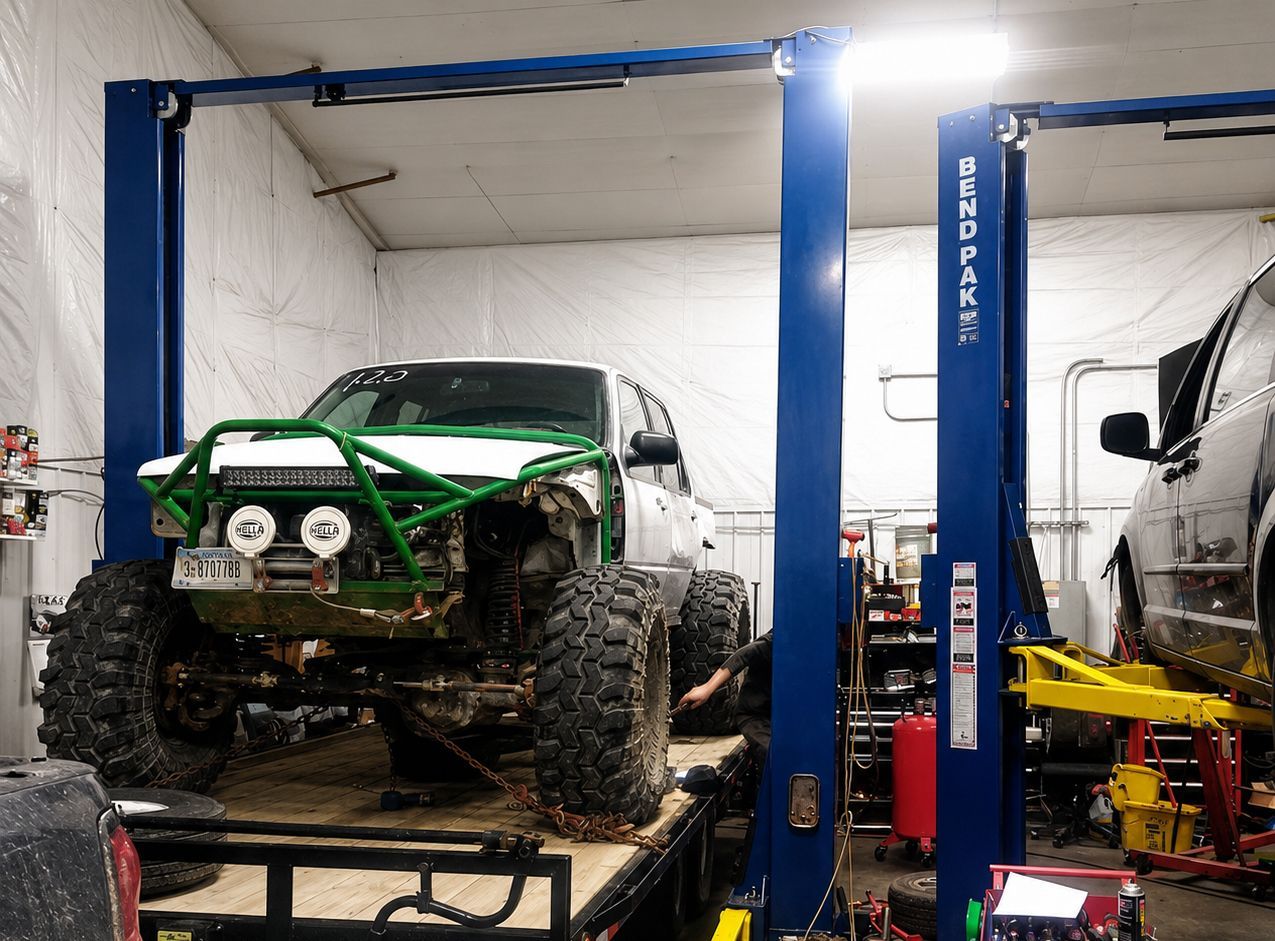 Green off-road vehicle on a lift in a garage workshop, with a van parked beside it.