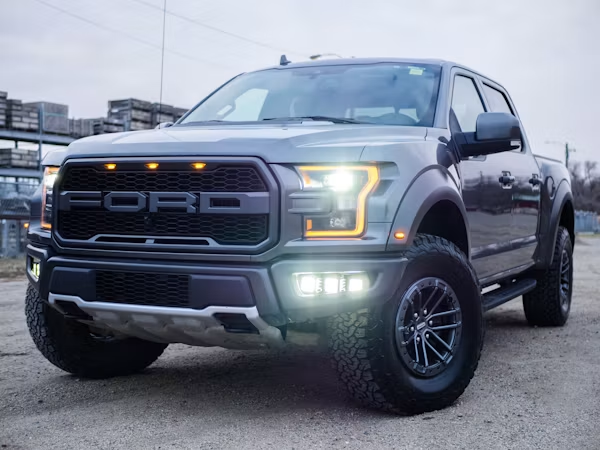 Gray Ford pickup truck parked on a wet lot, front view with headlights on