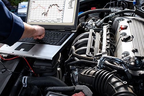 Mechanic using a laptop to diagnose a car engine in an open hood bay
