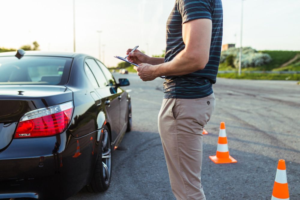 A Man Is Standing Next To A Car And Writing On A Clipboard — Darran Thompson Driver Training in Wollongong, NSW