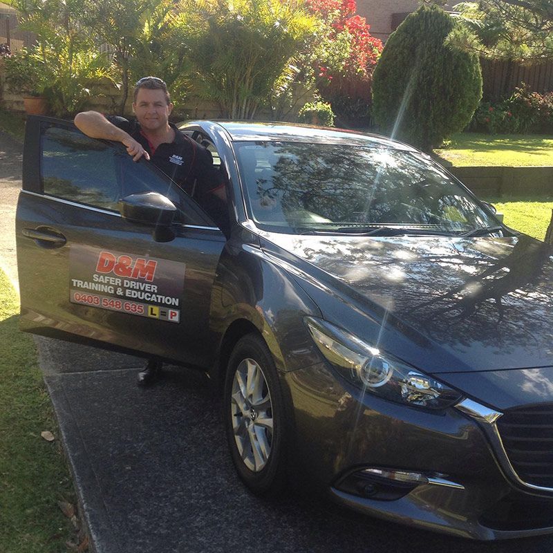 A Man Is Leaning On The Door Of A Car — Darran Thompson Driver Training in Wollongong, NSW