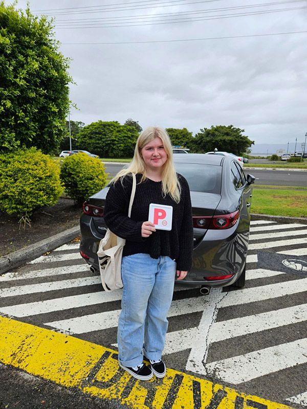 A Woman Is Standing In Front Of A Car Holding A P Letter Plate — Darran Thompson Driver Training in Wollongong, NSW