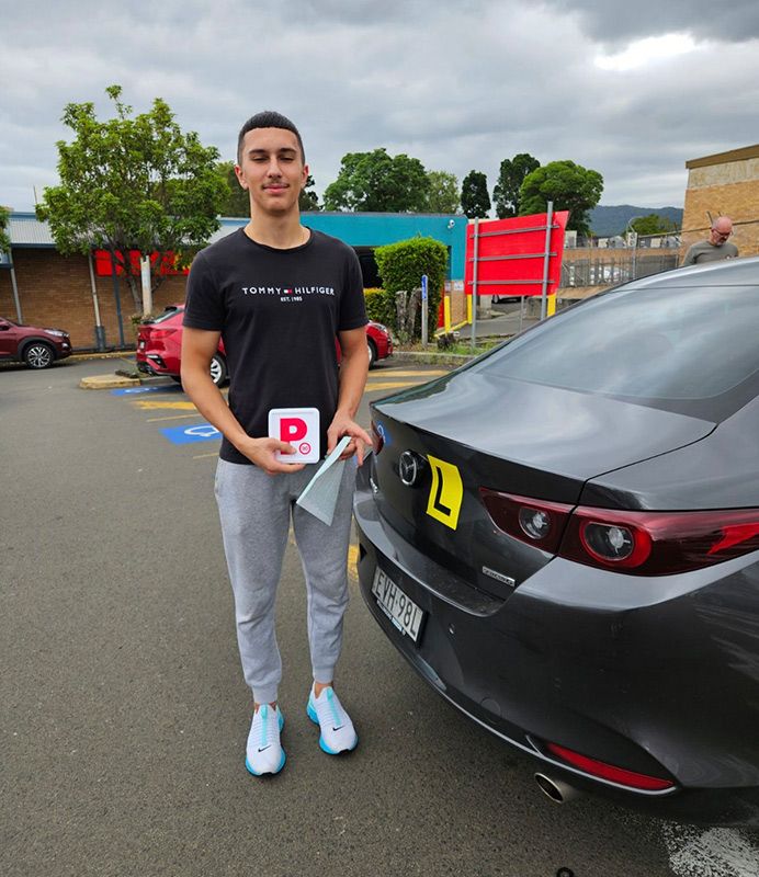 A Man Is Standing In Front Of A Car Holding Plate With The Letter P — Darran Thompson Driver Training in Wollongong, NSW