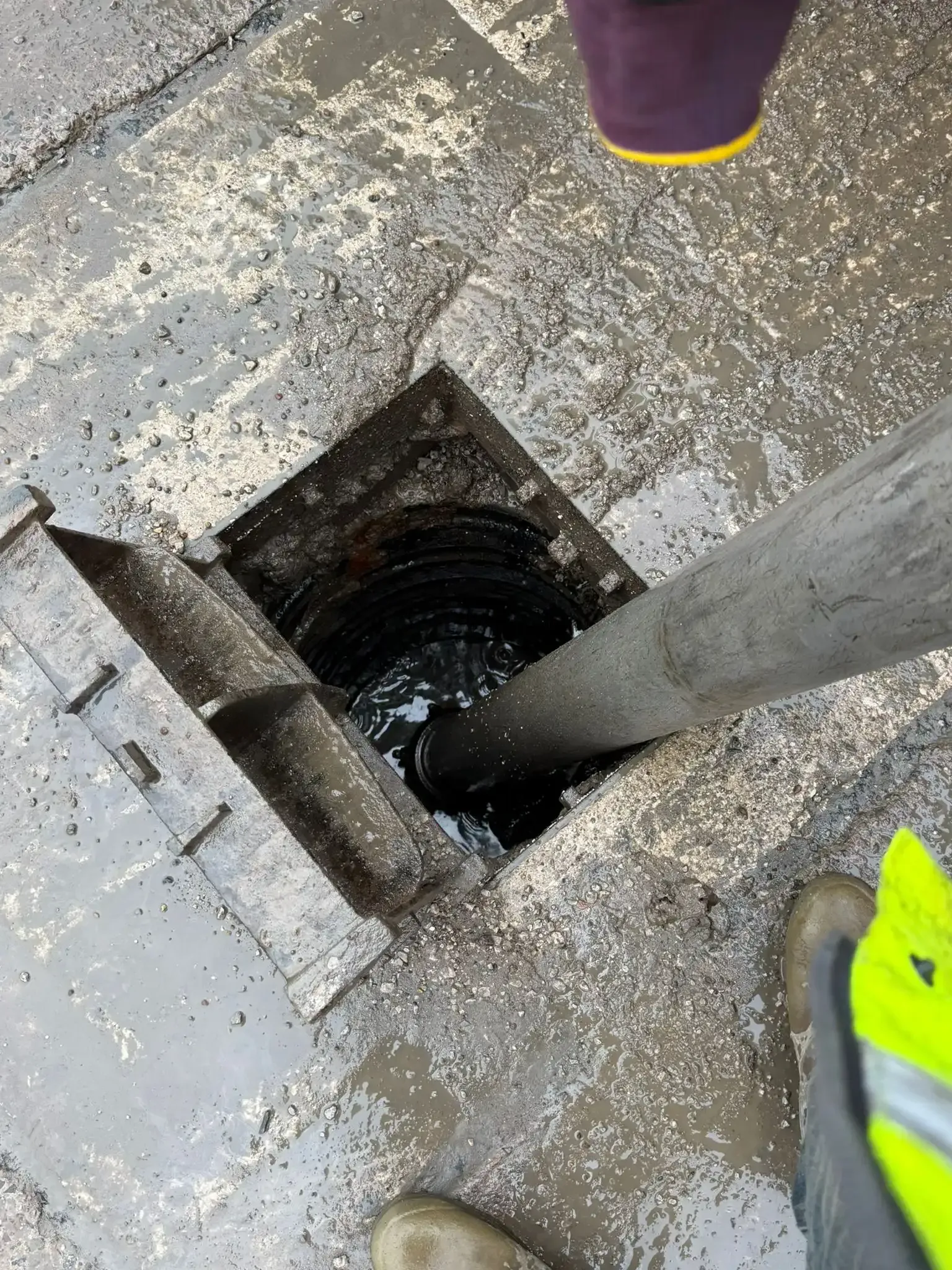 Grating drain in asphalt road, intersecting white painted lines.