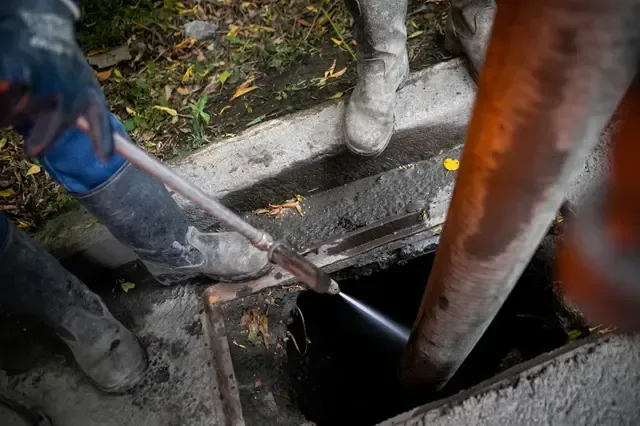 Workers using a hose to clean a sewer from an open manhole.