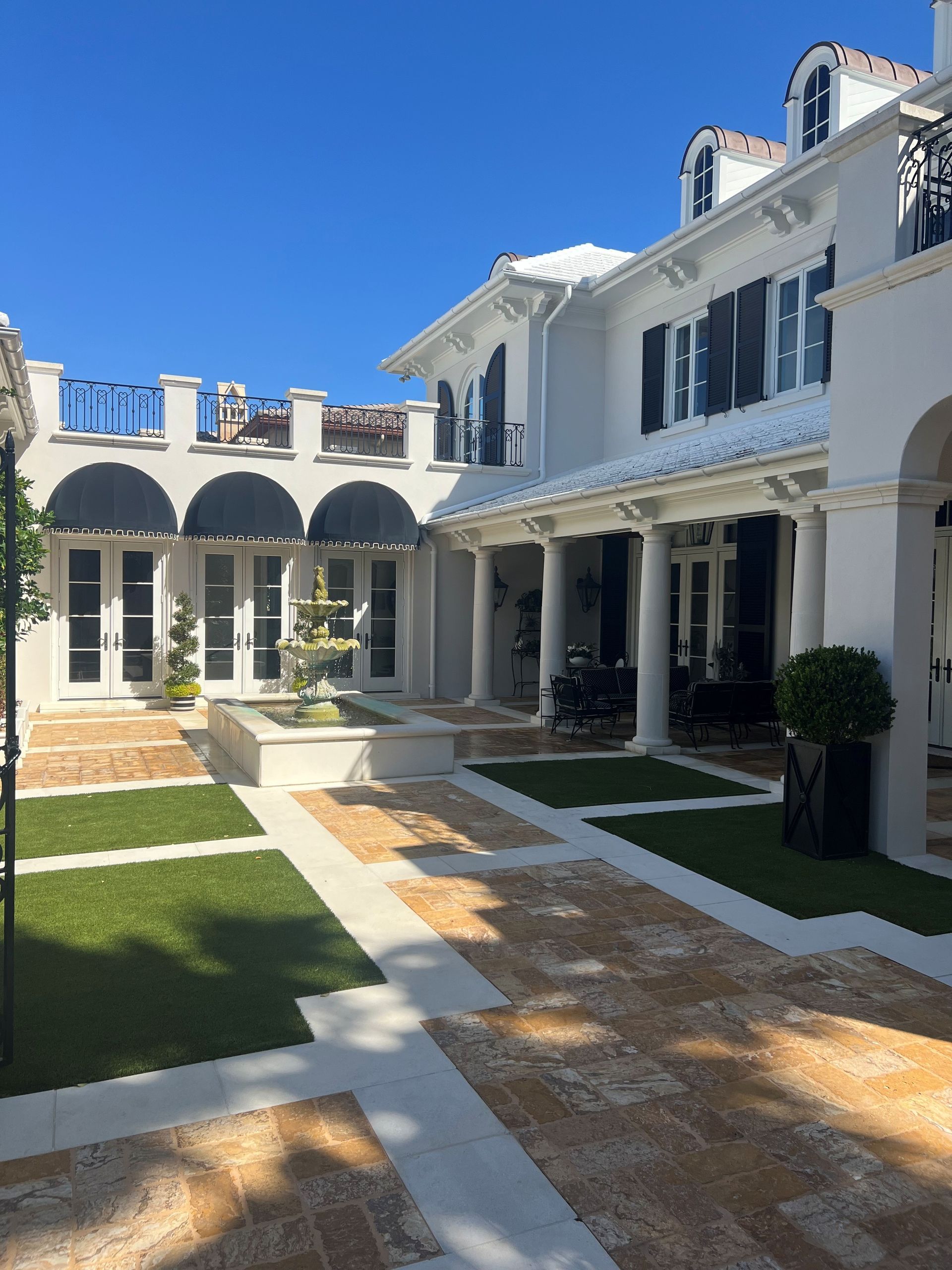 Bright white courtyard with arched windows, tiled paths, and manicured greenery under a sunny blue sky