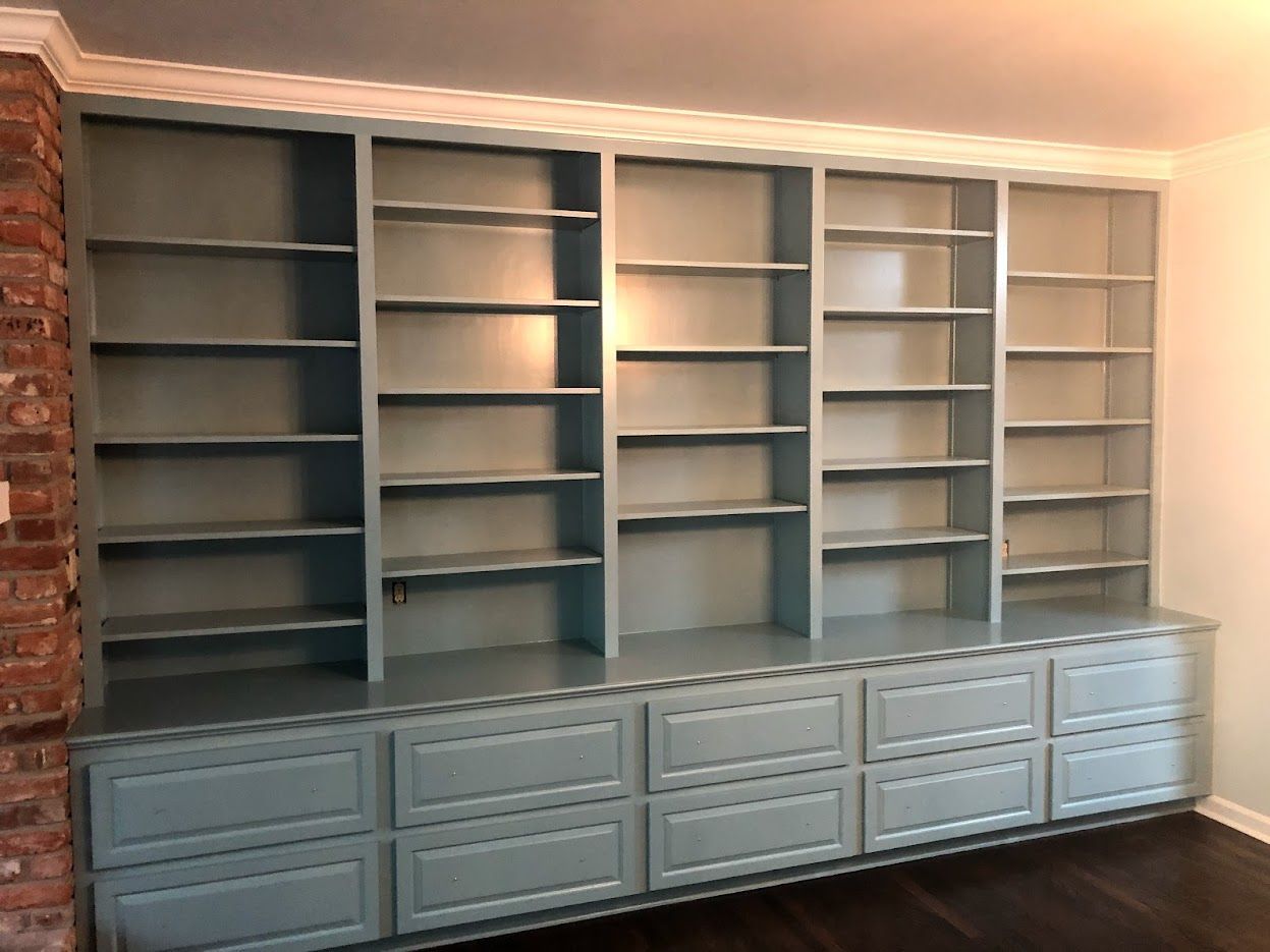 Wall-mounted built-in bookshelves with blue-gray shelves and drawers in a room with hardwood floors