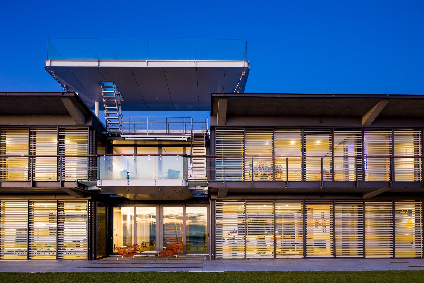 Modern glass-front office building with lit interior and rooftop terrace at dusk