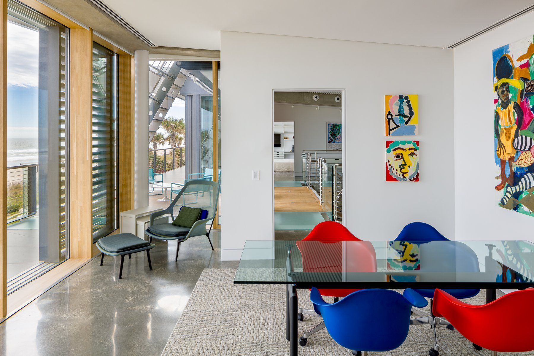 Modern beach house with palm trees, glass walls, and a green lawn under a blue sky.