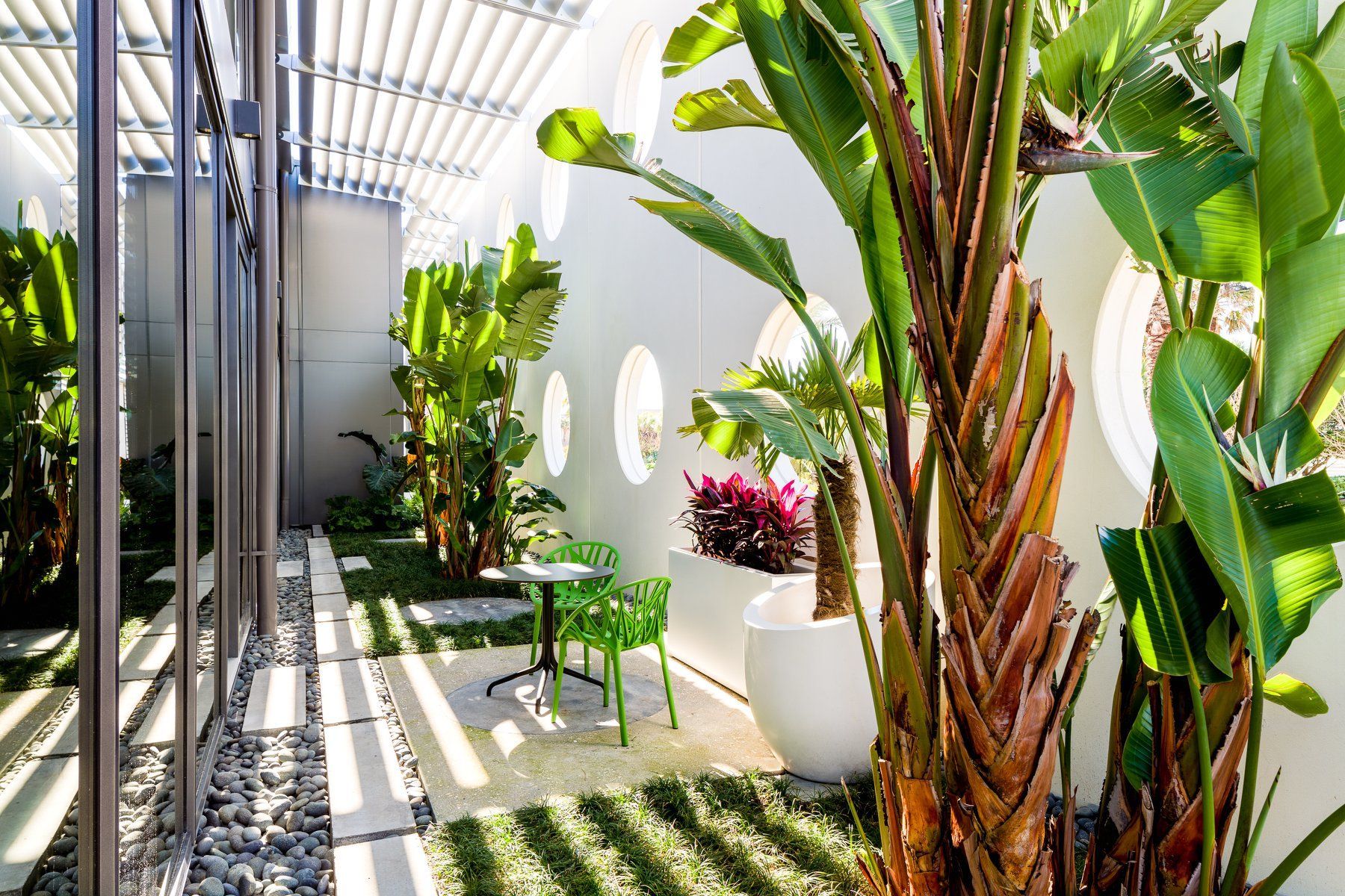 Outdoor patio with lush plants, white walls, and green table and chairs.