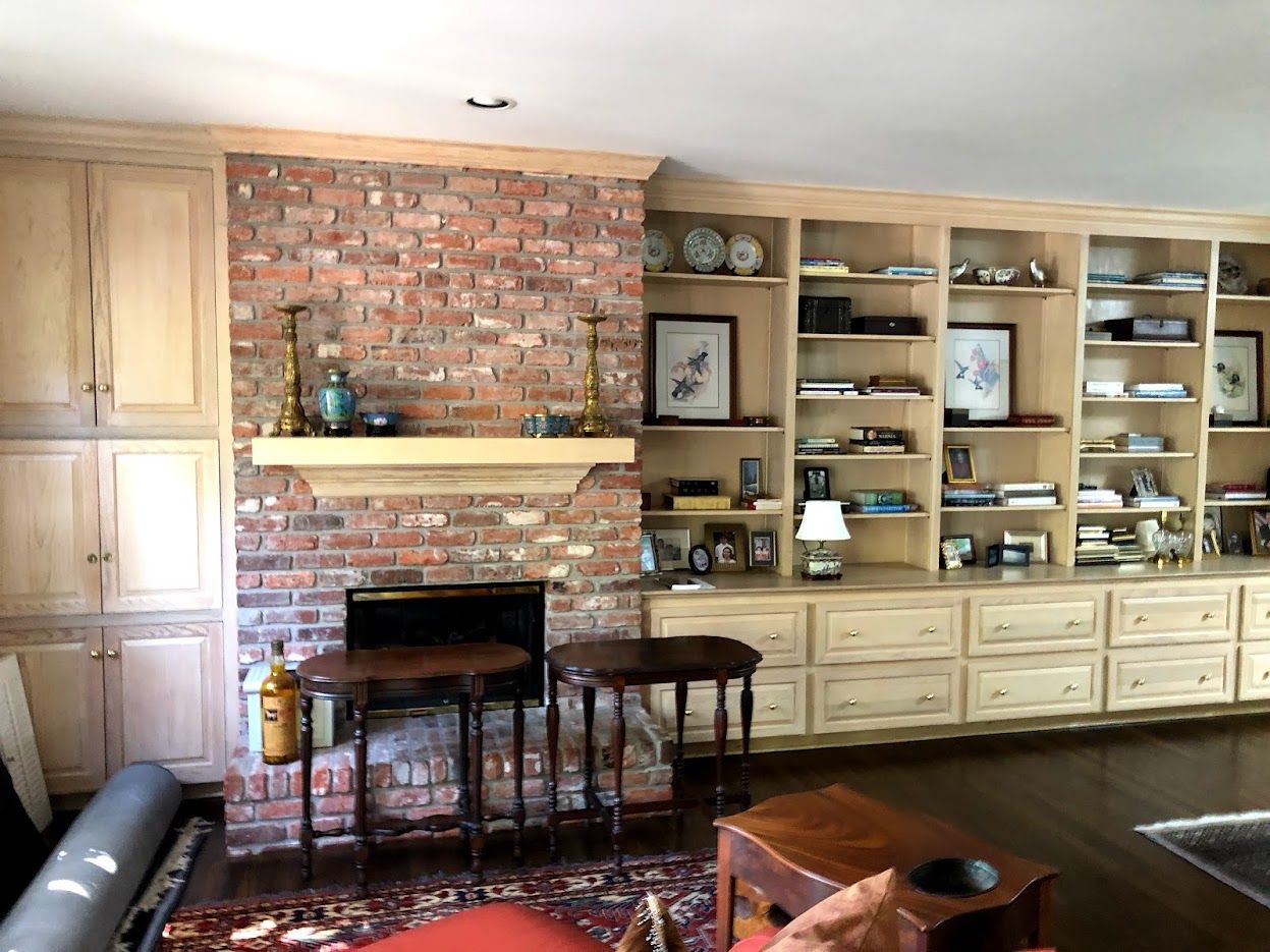 Living room with brick fireplace, built-in shelves, wooden cabinetry, and patterned rug