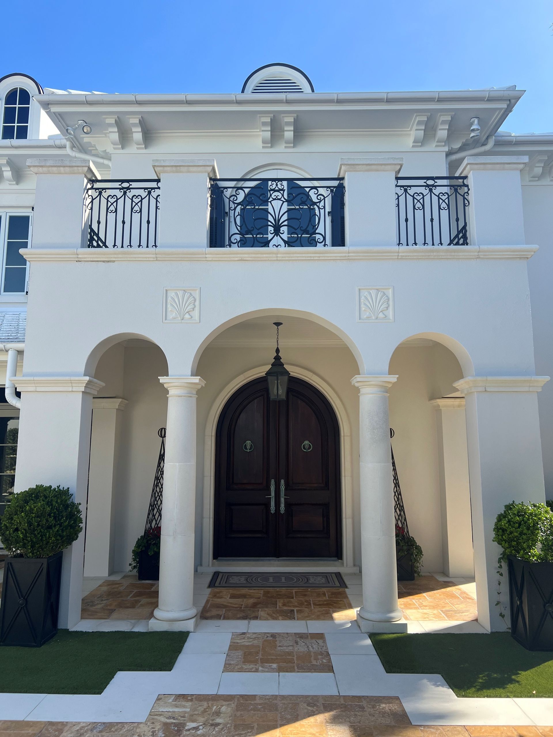White two-story house entrance with arched columns, dark double doors, and a small front walkway.