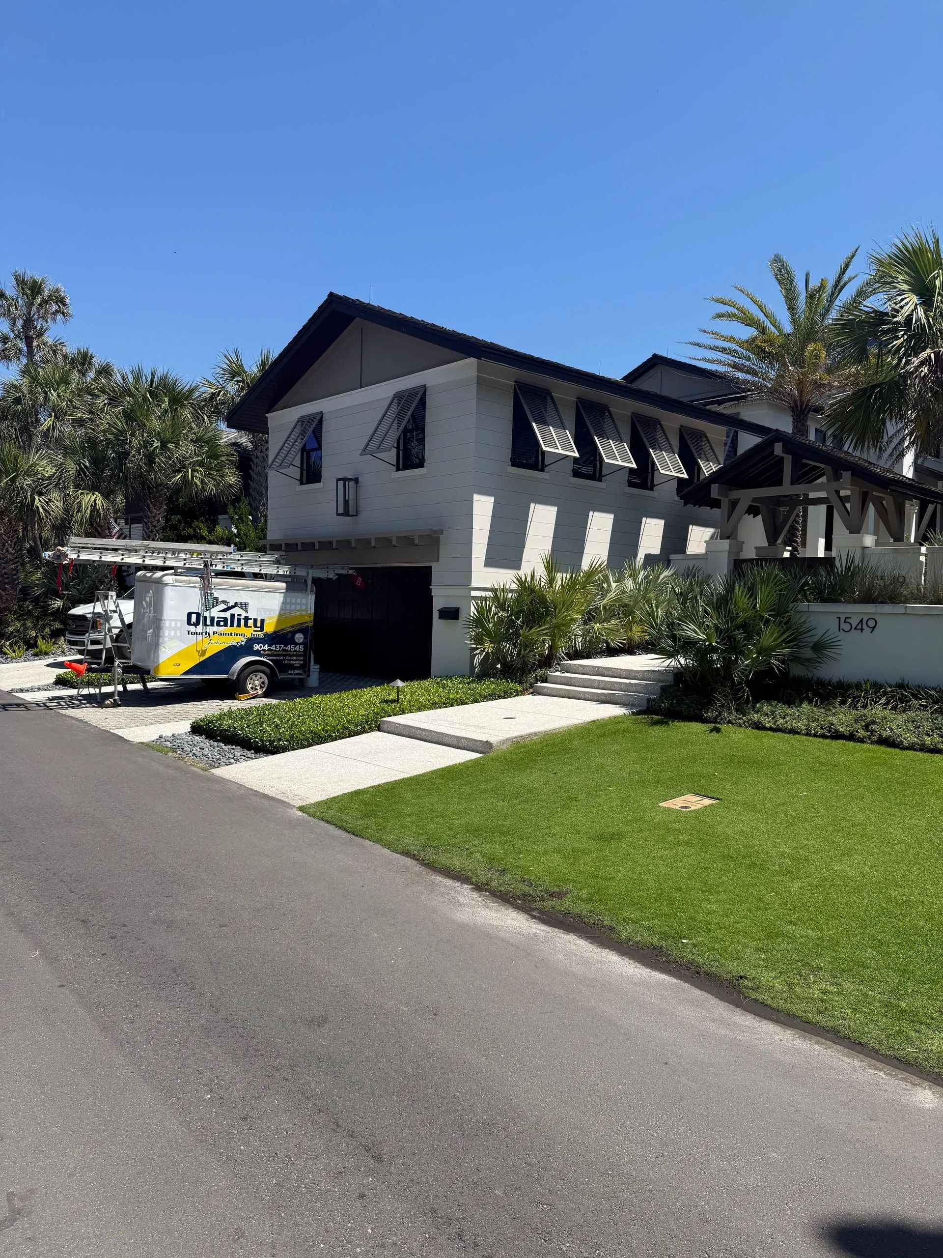 Two-story white house with black trim, driveway, lawn, and a white car parked under a carport on a sunny day