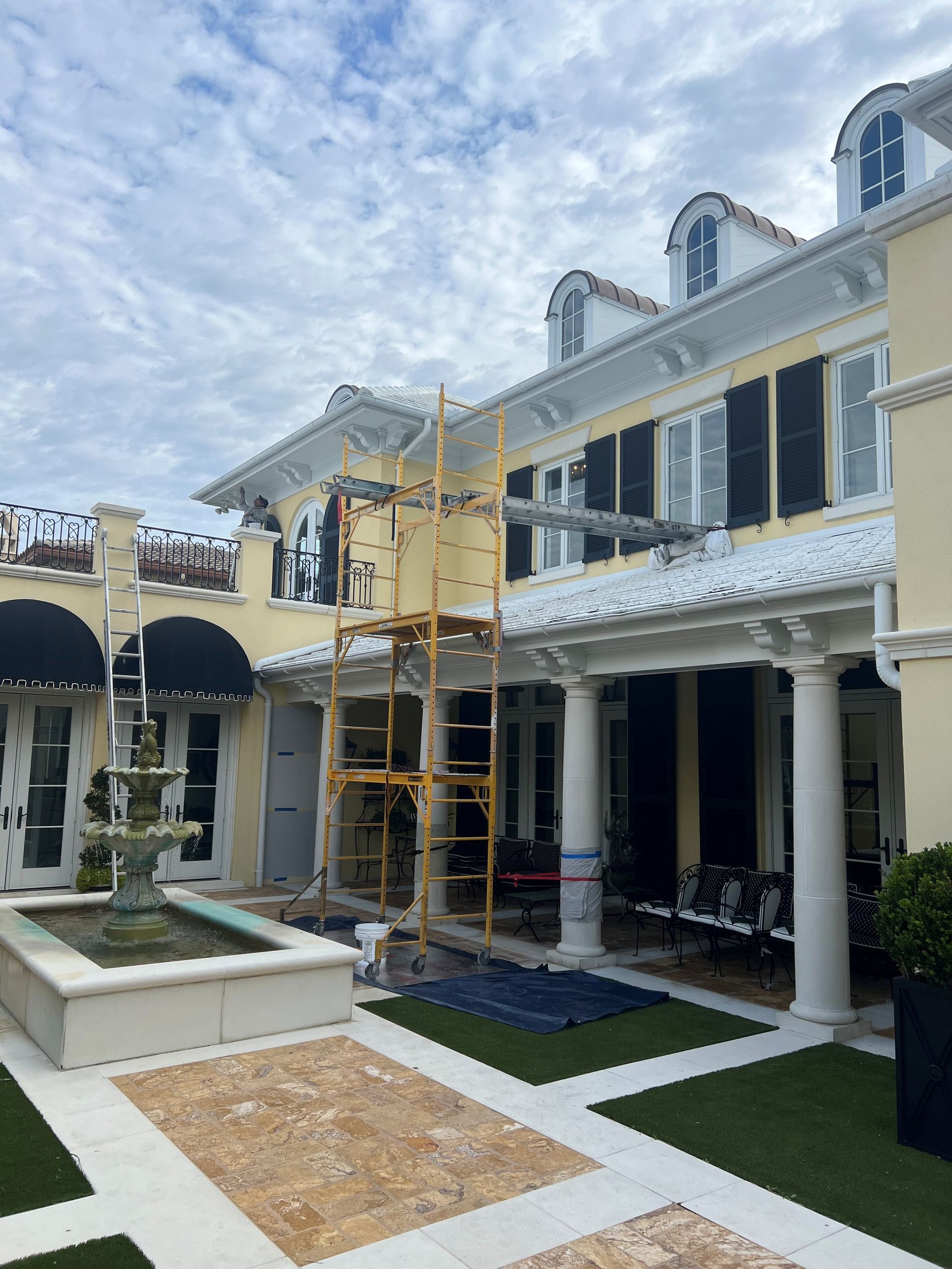 Luxury townhouse row under renovation, with yellow scaffolding in a courtyard and a partly cloudy sky.