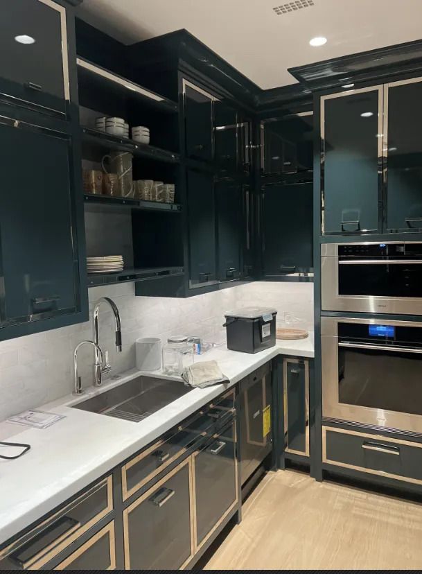 Dark modern kitchen with black cabinets, marble backsplash, and built-in oven next to a sink and countertop.