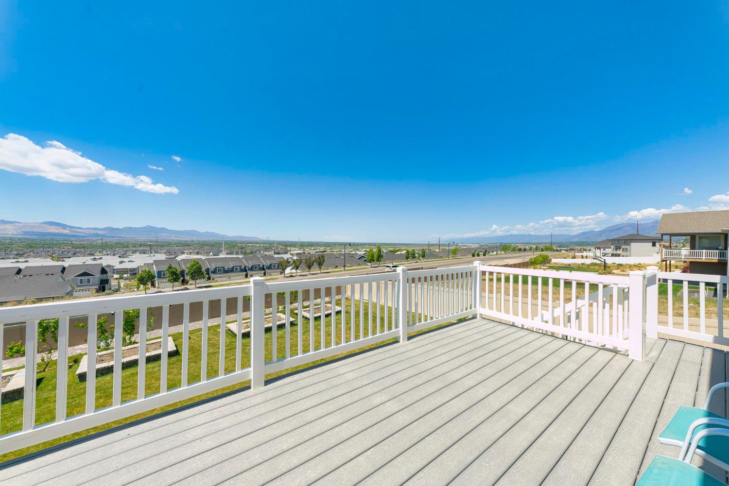 Sunny deck with white railing overlooking a valley and distant mountains under a bright blue sky