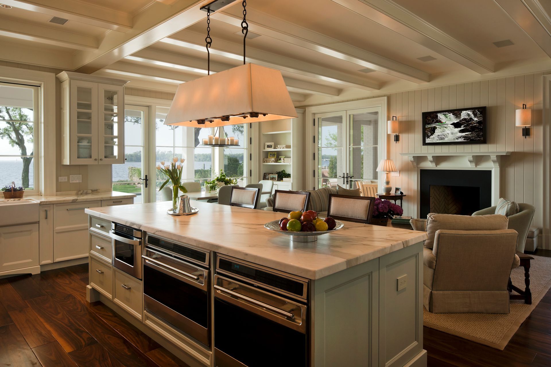 Spacious kitchen with island, appliances, and living area with fireplace; white and neutral tones, hardwood floors.