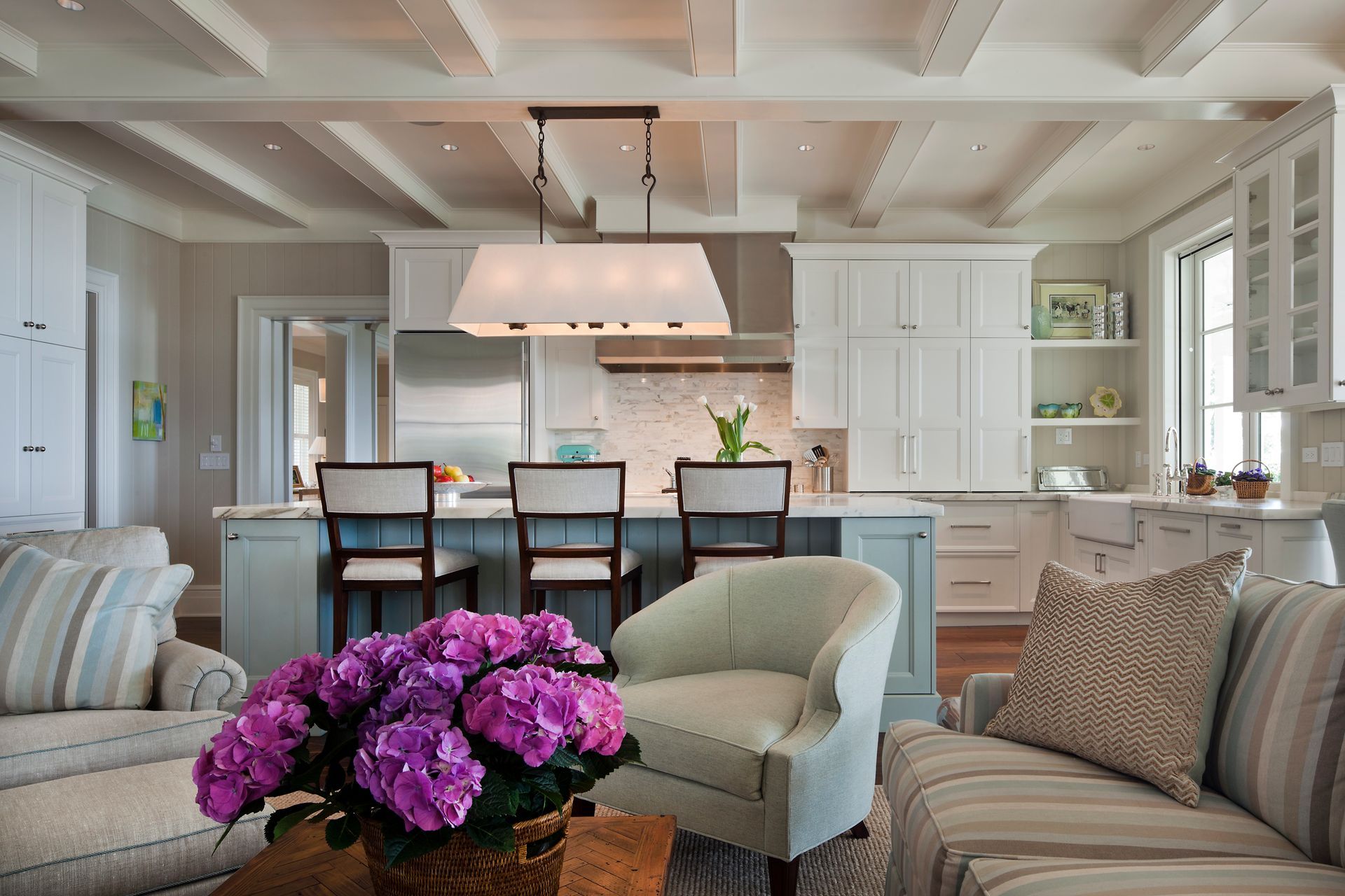 Coastal kitchen with blue and white cabinets, island, and exposed beams.