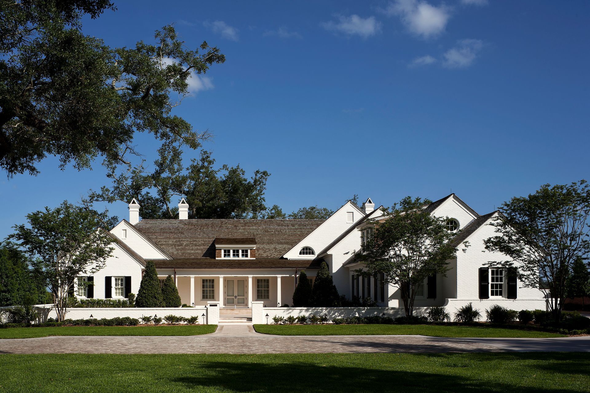 White farmhouse with a brown roof, shutters, and a stone driveway under a blue sky.