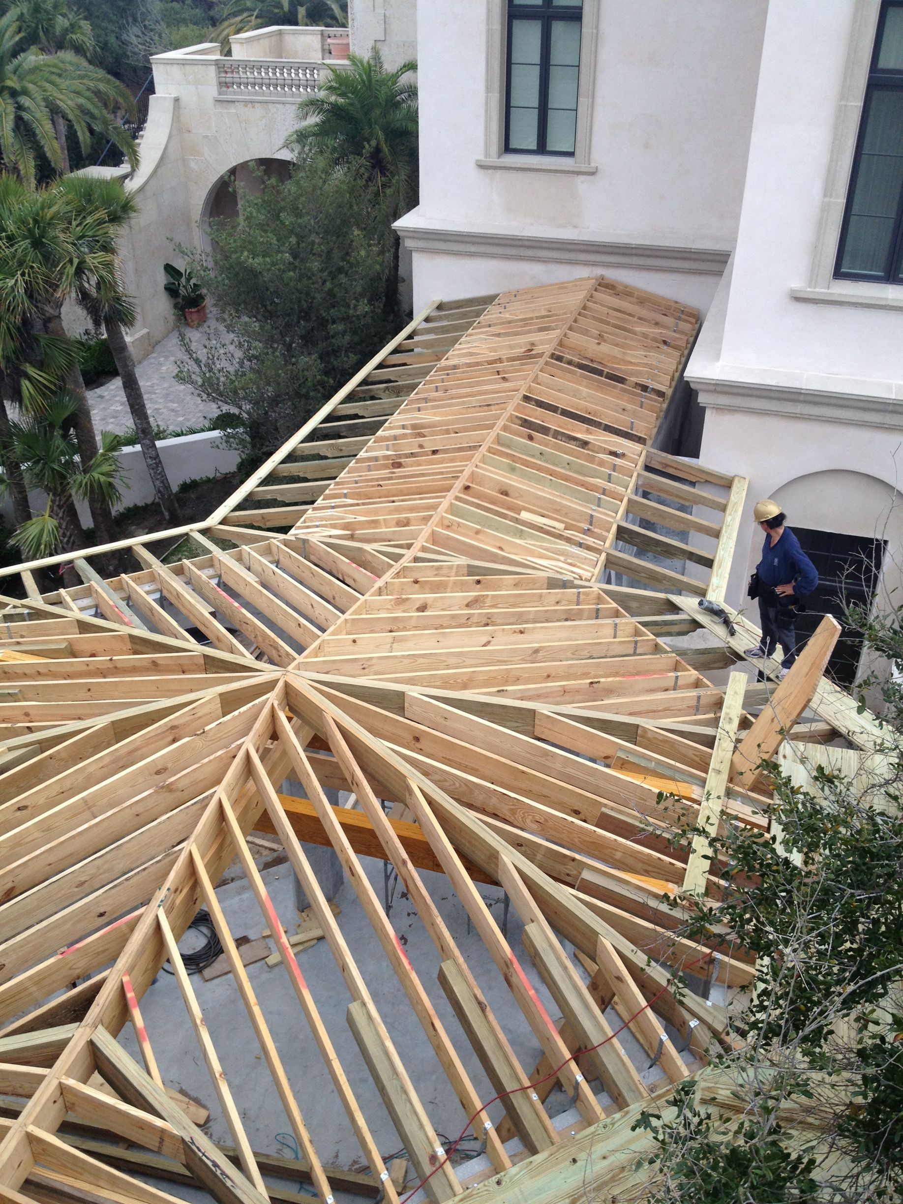 Construction of a wooden roof frame on a white building. A worker stands on the edge. Outdoors, sunny day.