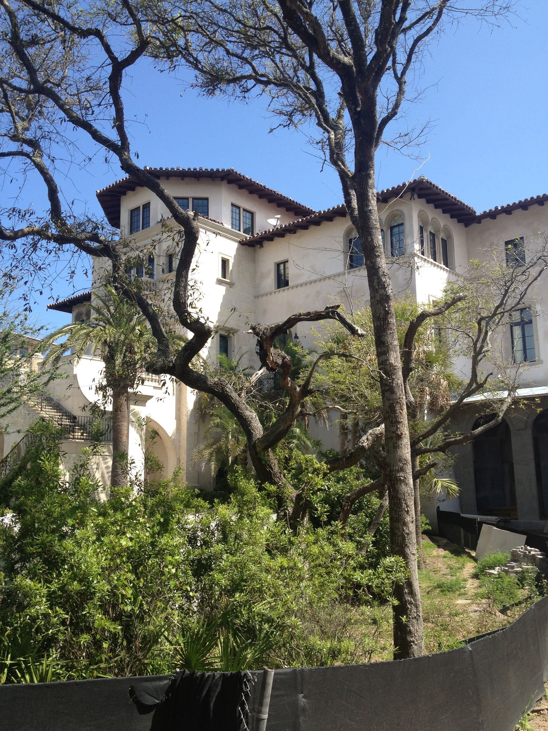 White stucco building with a red tile roof, framed by tree branches. Sunny day.
