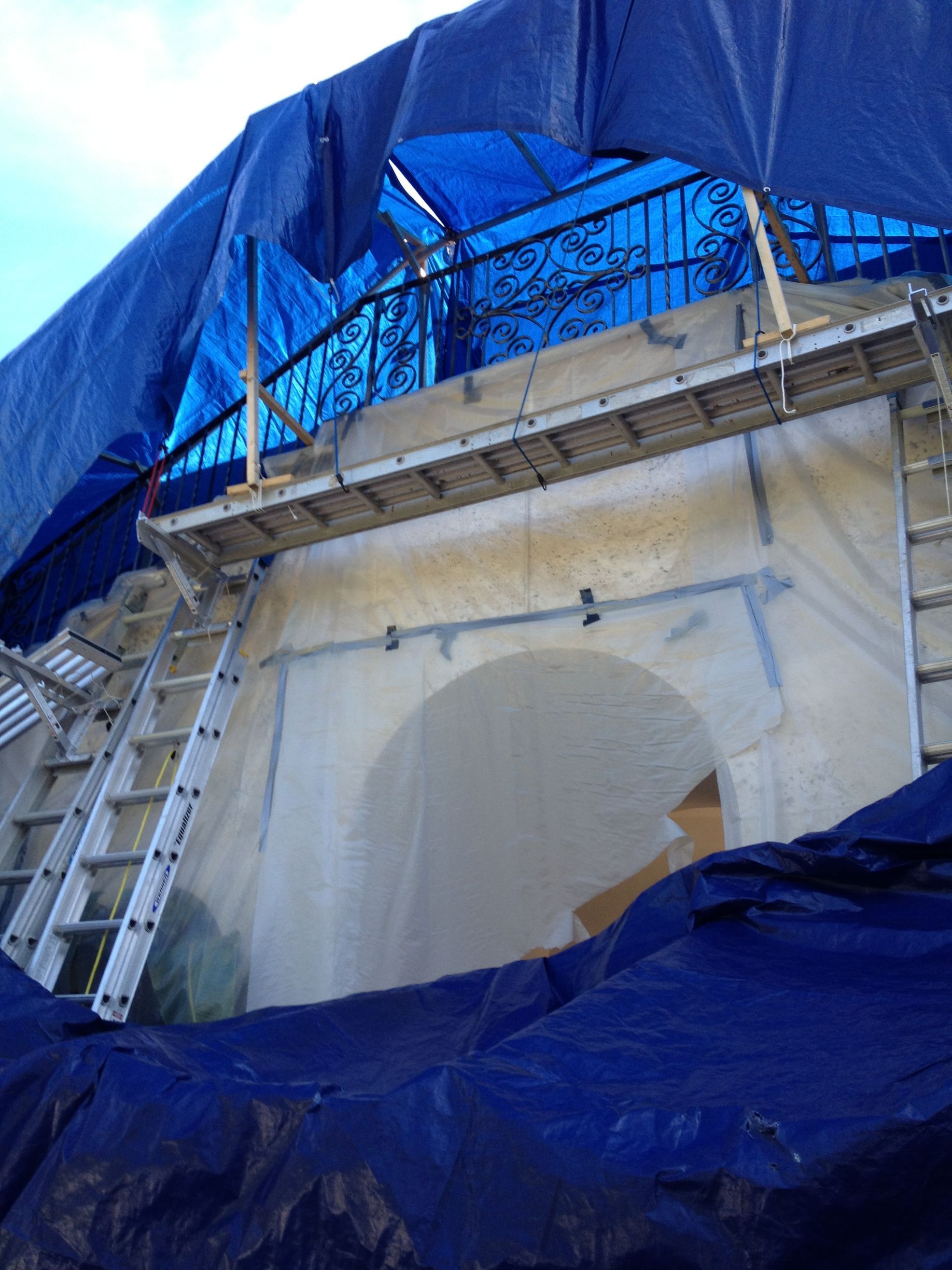 Building under repair, covered in blue tarps and scaffolding; arched doorway visible.