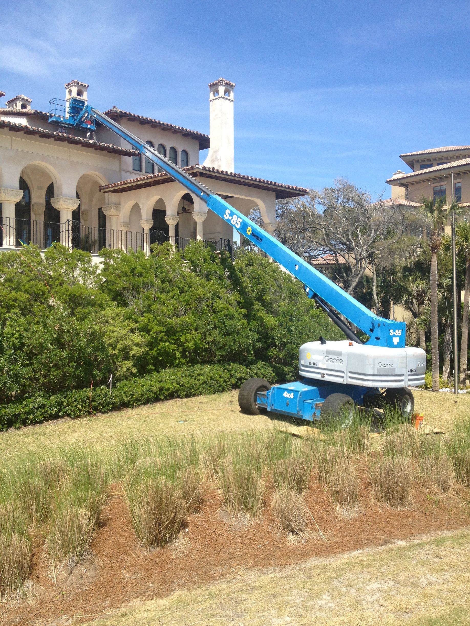 A blue boom lift servicing a large, ornate building on a sunny day.