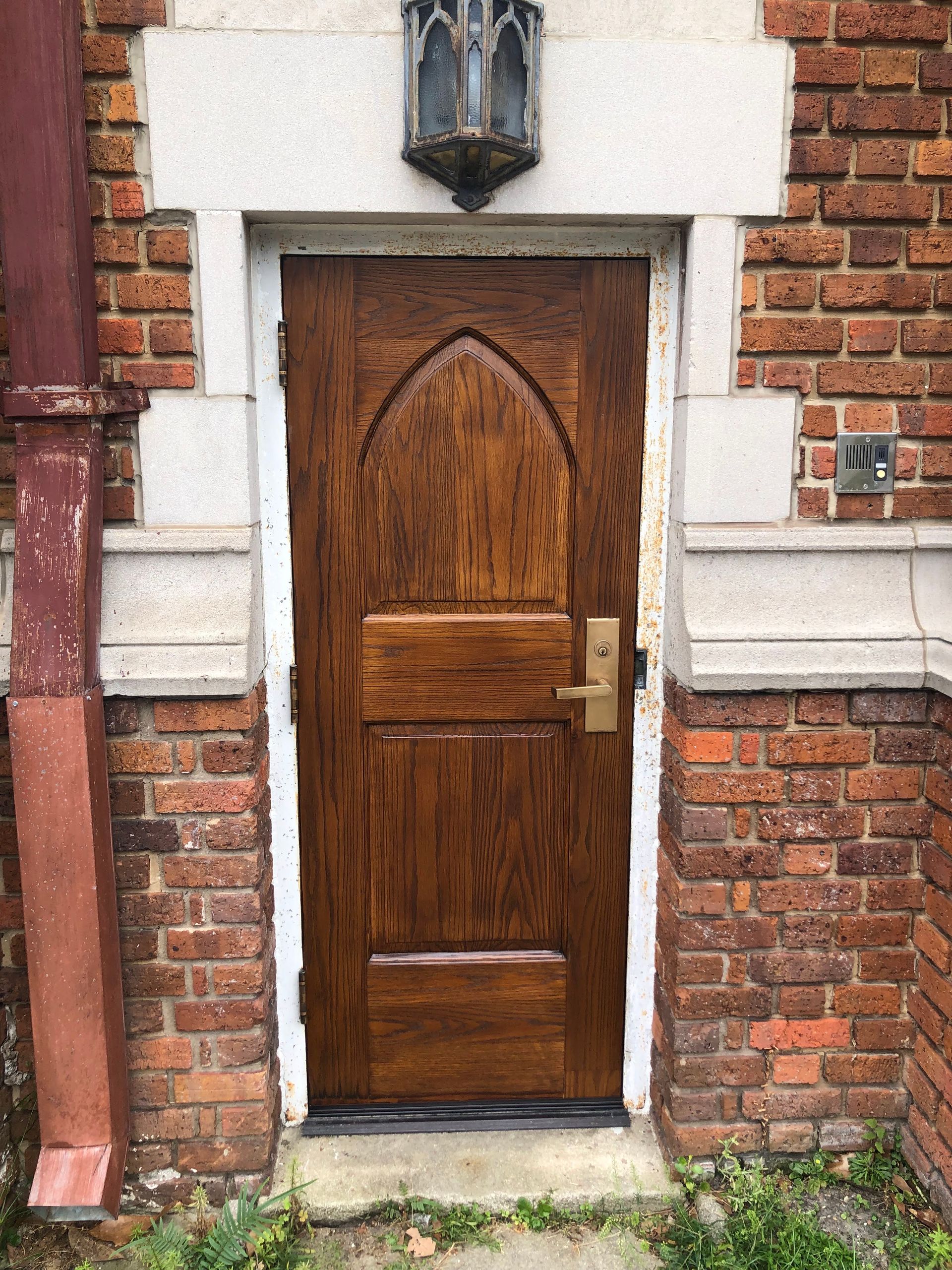 Wooden arched door, brass hardware, brick building exterior, stone trim, outdoor.